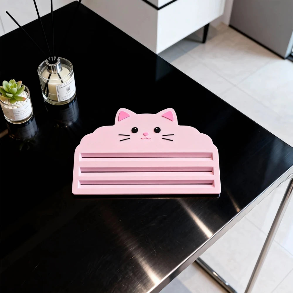 A pink cat face squeezer tool rests on a black table next to a glass jar.