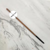 A long, slender wooden wand with a metal core is displayed on a white marble surface.