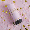 A pink hand twist confetti cannon is shown surrounded by loose pink and gold confetti petals.