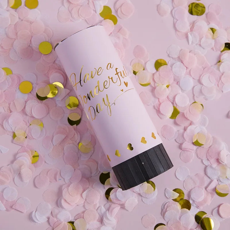 A pink hand twist confetti cannon is shown surrounded by loose pink and gold confetti petals.
