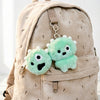 A light beige backpack featuring a green plush keychain with a clear photocard holder attached.