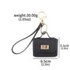 A black mini leather openable bag keychain with a gold-tone clasp and attached black cord.