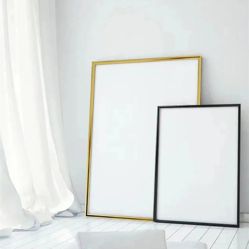A framed piece of white art or print with a gold frame and a separate black frame leaning against a white wall.