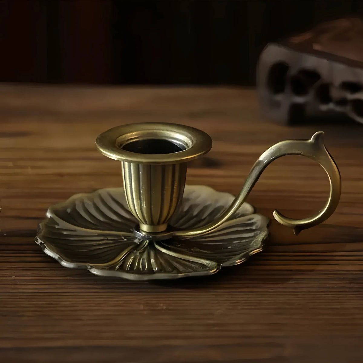 Un photophore lotus en fer forgé vintage avec une base en laiton repose sur une surface en bois.