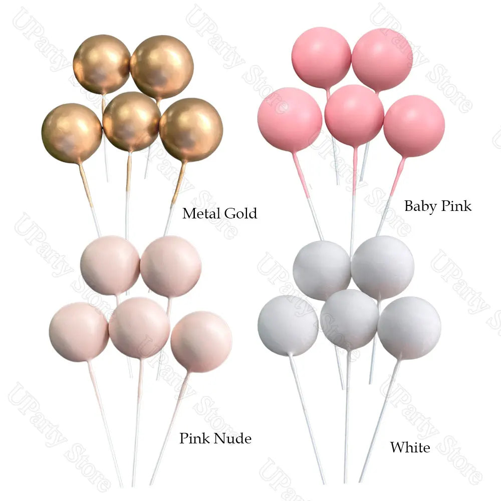 A set of boho rainbow cake toppers featuring gold, pink, nude, and white ball decorations on sticks.