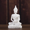 White handcrafted resin Buddha statue seated in meditation on a wooden surface.