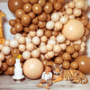 A large arrangement of sand and beige latex balloons with a cake, a tiger, and a baby sitting in front.
