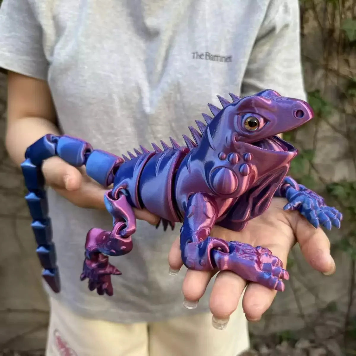 A hand holds a purple and blue articulated 3D printed lizard figurine for home decor.