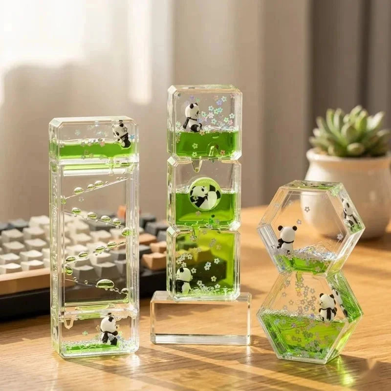 A glass hourglass timer filled with green liquid and small panda figurines, used as desk decor.