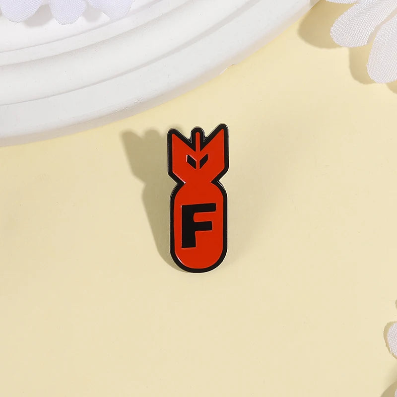 An enamel pin featuring an orange shark head design with the letter F on a light yellow background.