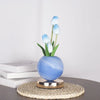 A light blue tulip flower arrangement in a blue ceramic vase on a woven mat.