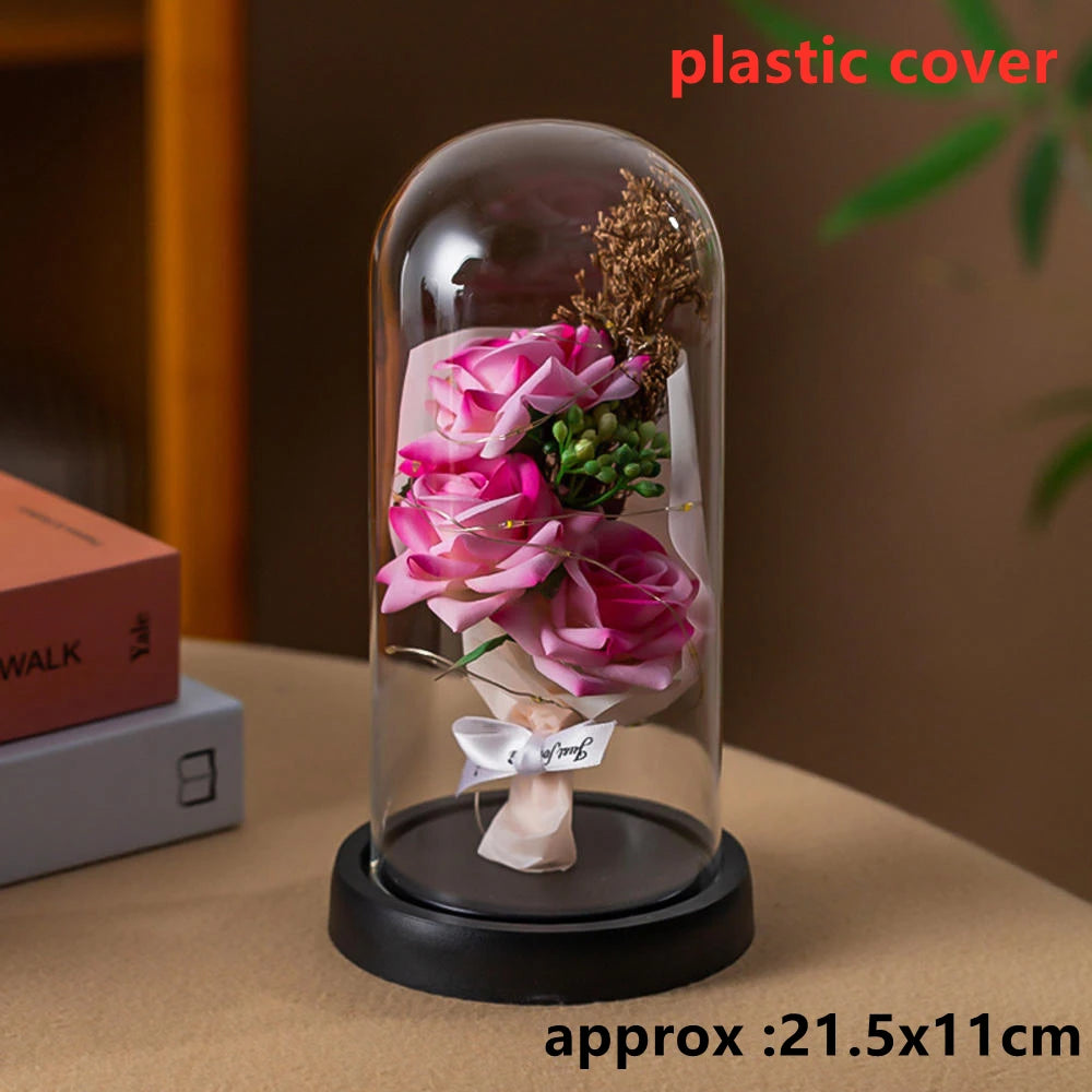 A glass dome display featuring a pink rose and dried floral elements on a black base.