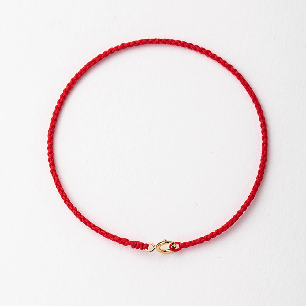 A handmade red string bracelet with a gold plated clasp laid flat on a white background.