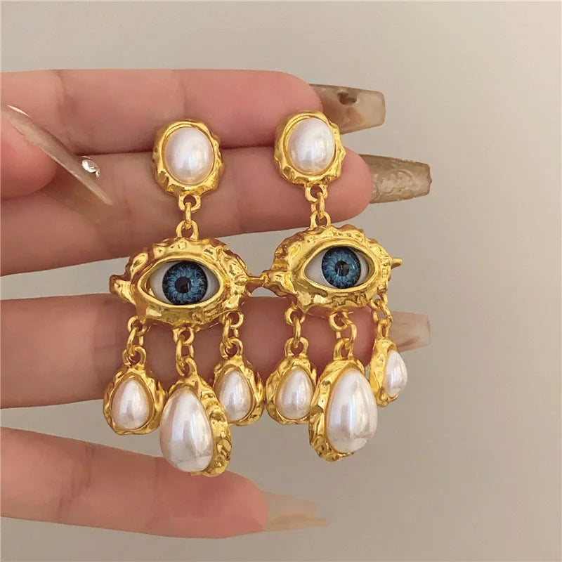 Gold-toned pearl drop earrings featuring a central blue eye design and multiple white pearls.