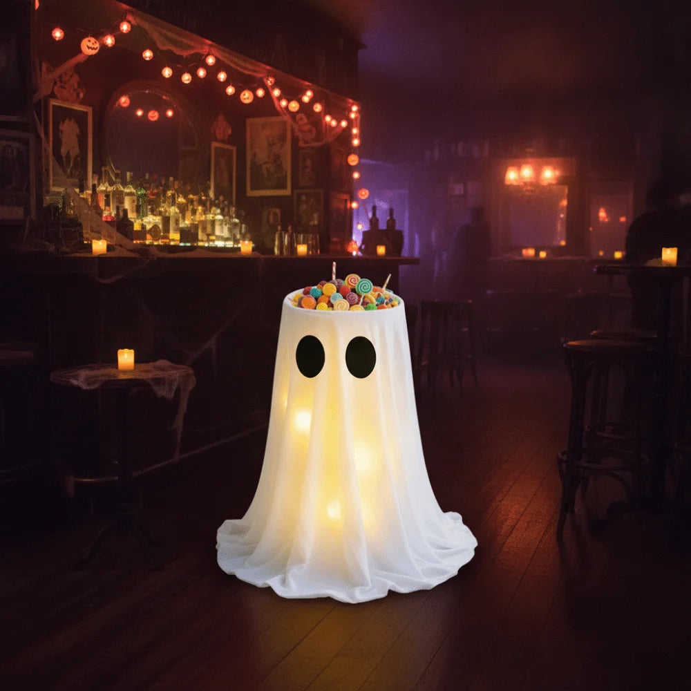 A white glowing ghost shaped bucket filled with colorful Halloween treats sits on a wooden floor in a dimly lit bar setting.