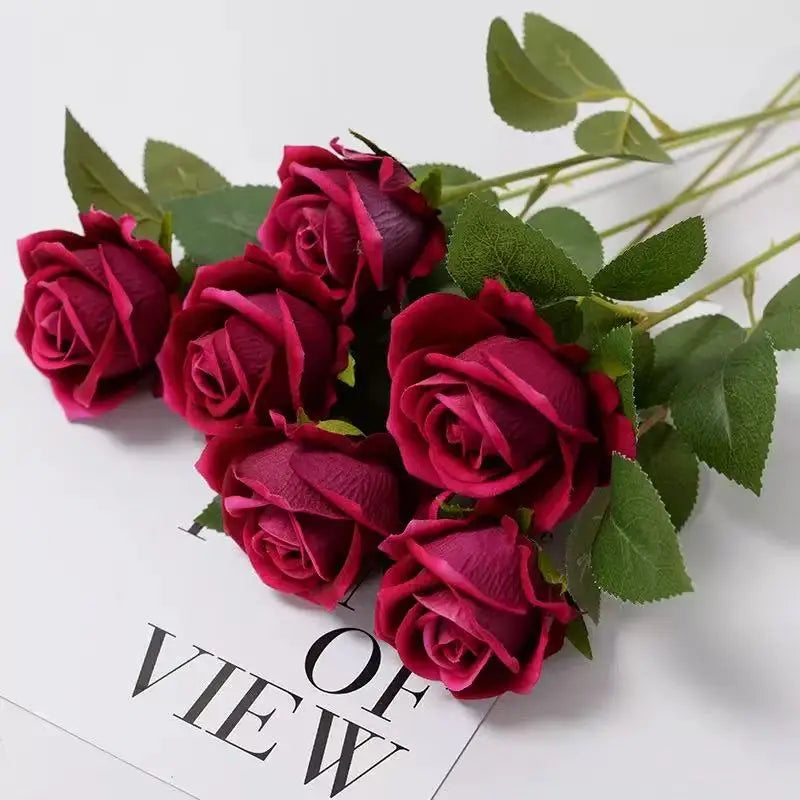 A bouquet of deep magenta velvet artificial roses with green leaves shown from a top-down view.