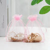 Pink organza drawstring gift bags filled with assorted jewelry and small items