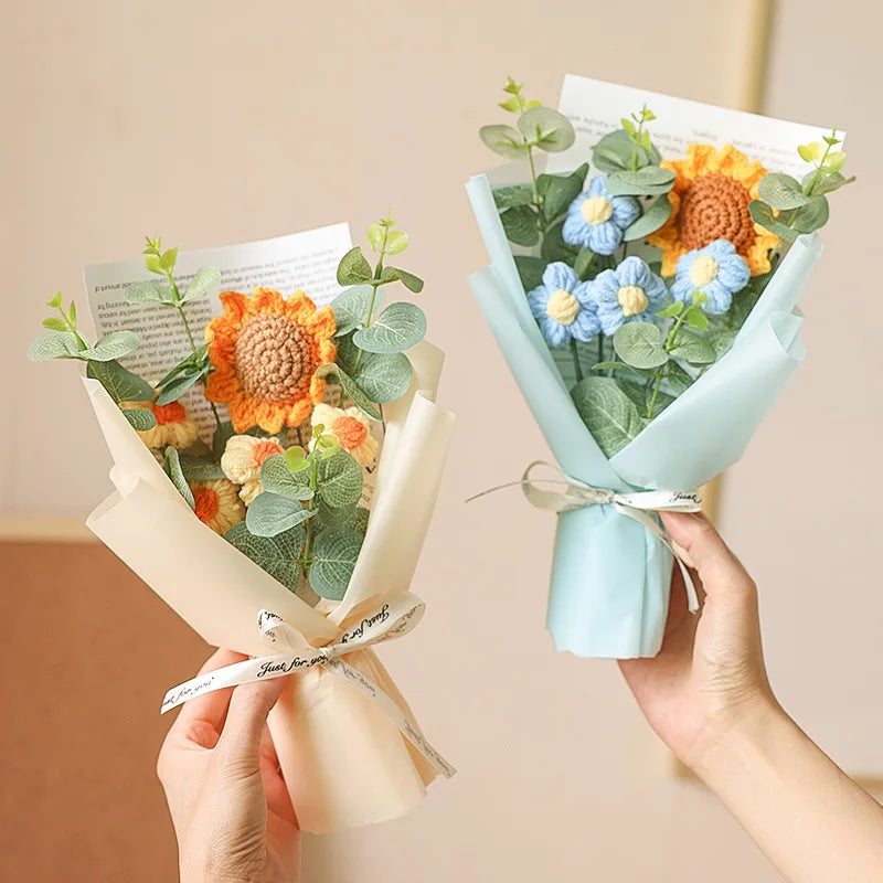 A hand holds a bouquet of handcrafted crochet sunflowers and greenery wrapped in light blue paper.