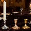 A vintage brass iron candlestick holder for table centerpieces is placed on a dark velvet tablecloth.