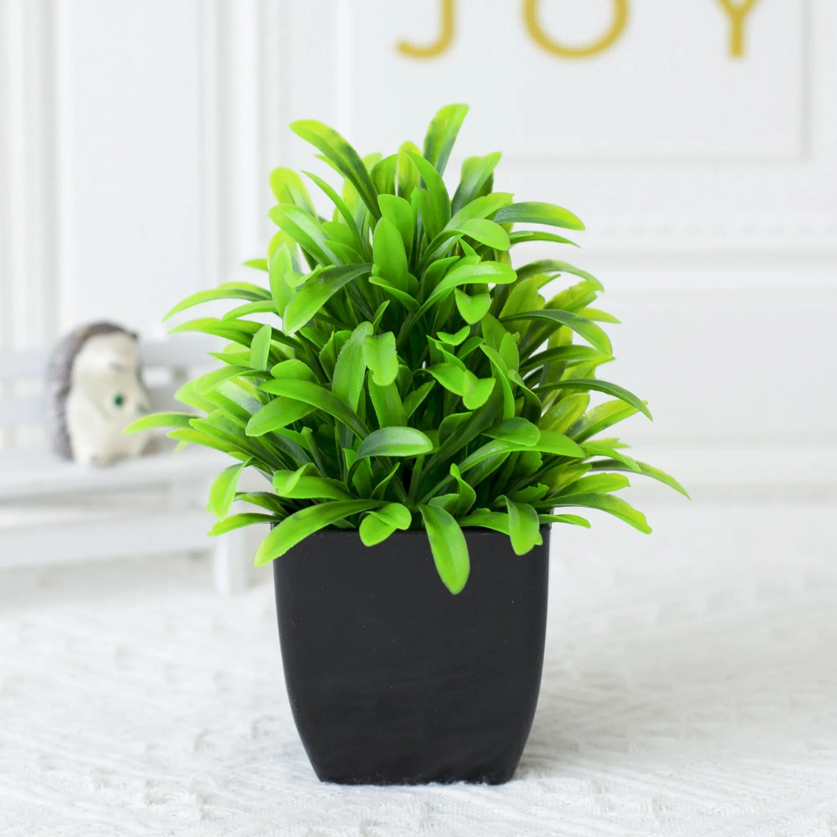 A vibrant green artificial eucalyptus potted plant in a black pot on a white surface.