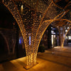 Instalación decorativa con una gran estructura de árbol dorado cubierta de luces LED blancas cálidas.