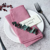 A stack of pink textured linen napkins with a gold tag reading Romance First placed on a white plate.