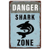 A vintage distressed tin sign with the text DANGER SHARK ZONE on a blue background.