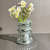 A vase filled with white daisies sits on a surface, surrounded by stacked silver mirror tiles.