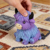 A purple and blue Scottish Highland cow squishy stress relief toy being held by a hand.