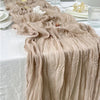 A flowing, semi-sheer gauze table runner in sage green fabric draped on a white tablecloth.