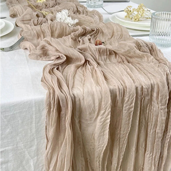 A flowing, semi-sheer gauze table runner in sage green fabric draped on a white tablecloth.