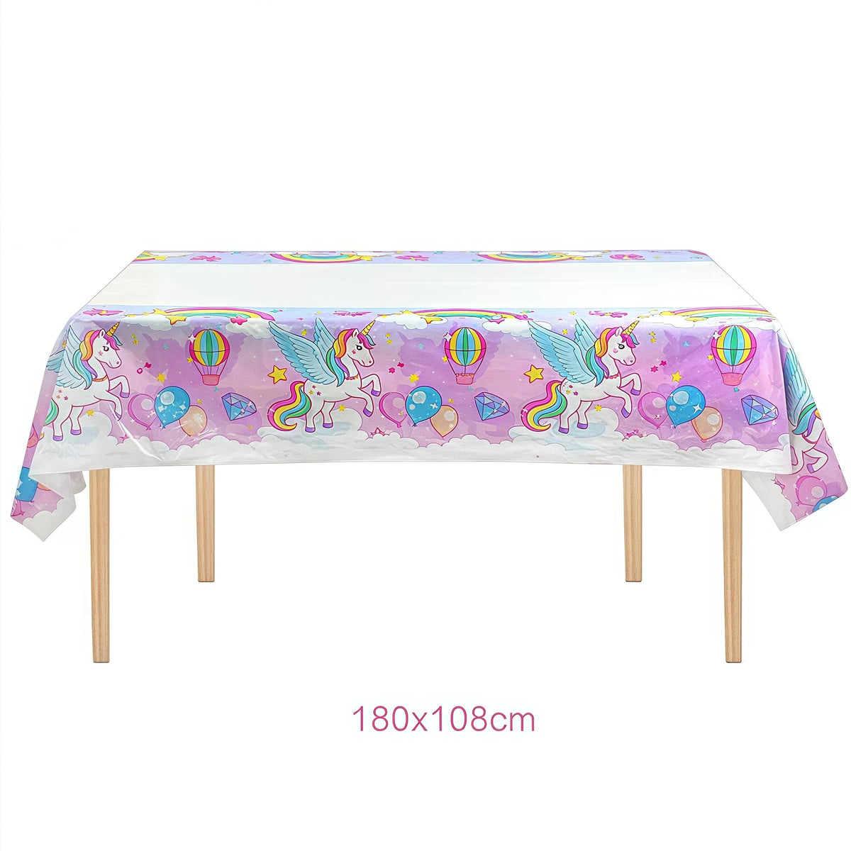 A white table covered with a colorful unicorn themed tablecloth featuring unicorns and balloons for a birthday party.