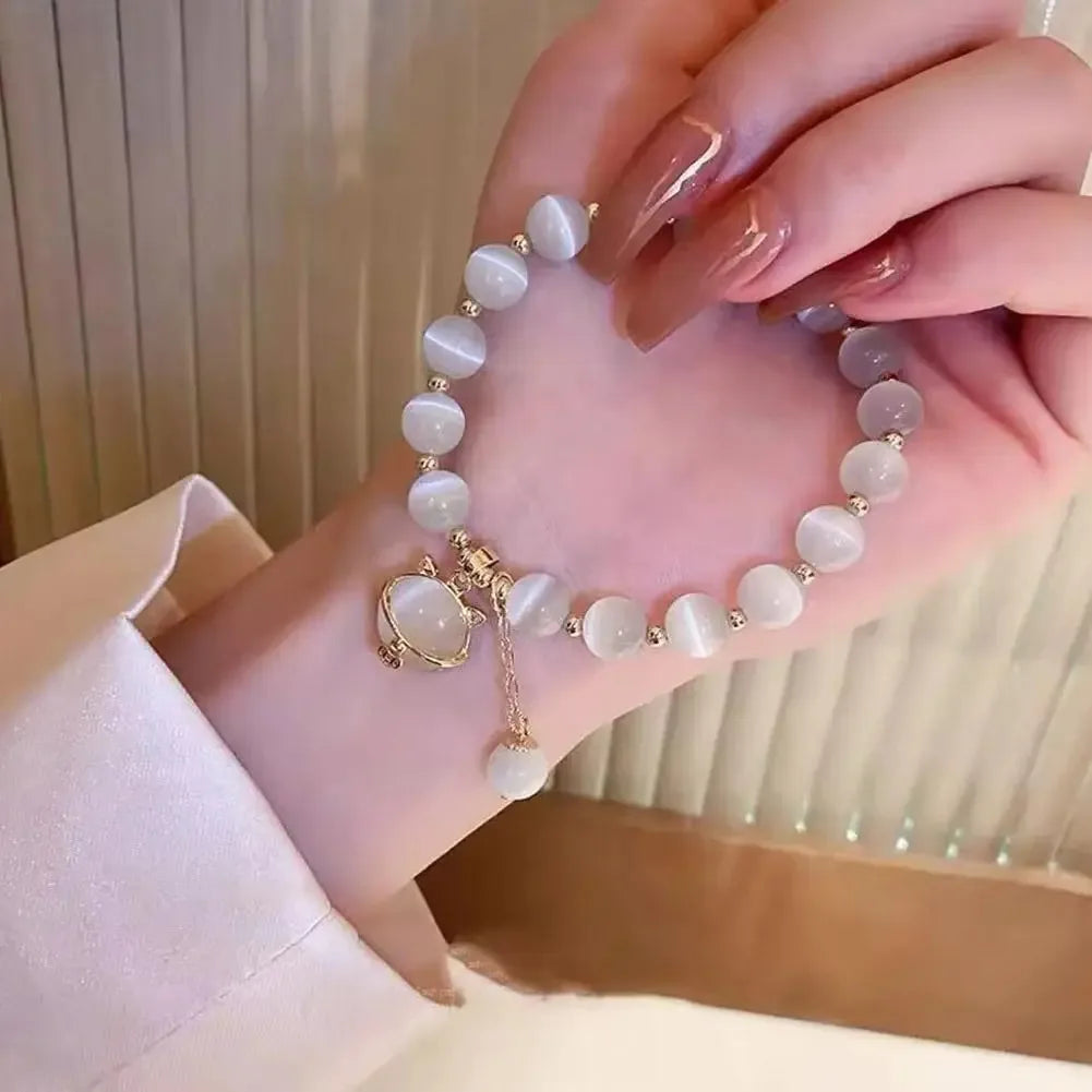 A hand wearing a delicate bracelet made of small, round, pale pink natural stones and a gold charm.
