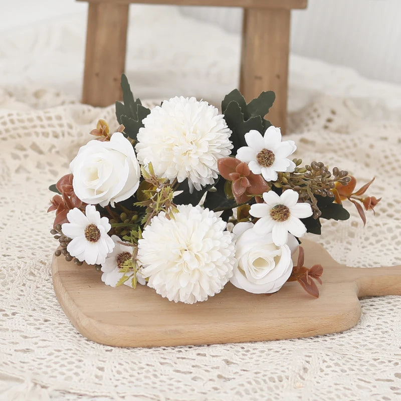 A bouquet of white and dusty rose silk flowers, including roses and hydrangeas, arranged on a wooden board.