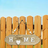 A wooden welcome sign with the words HOME carved into a plank, hanging on a vertical wooden fence.