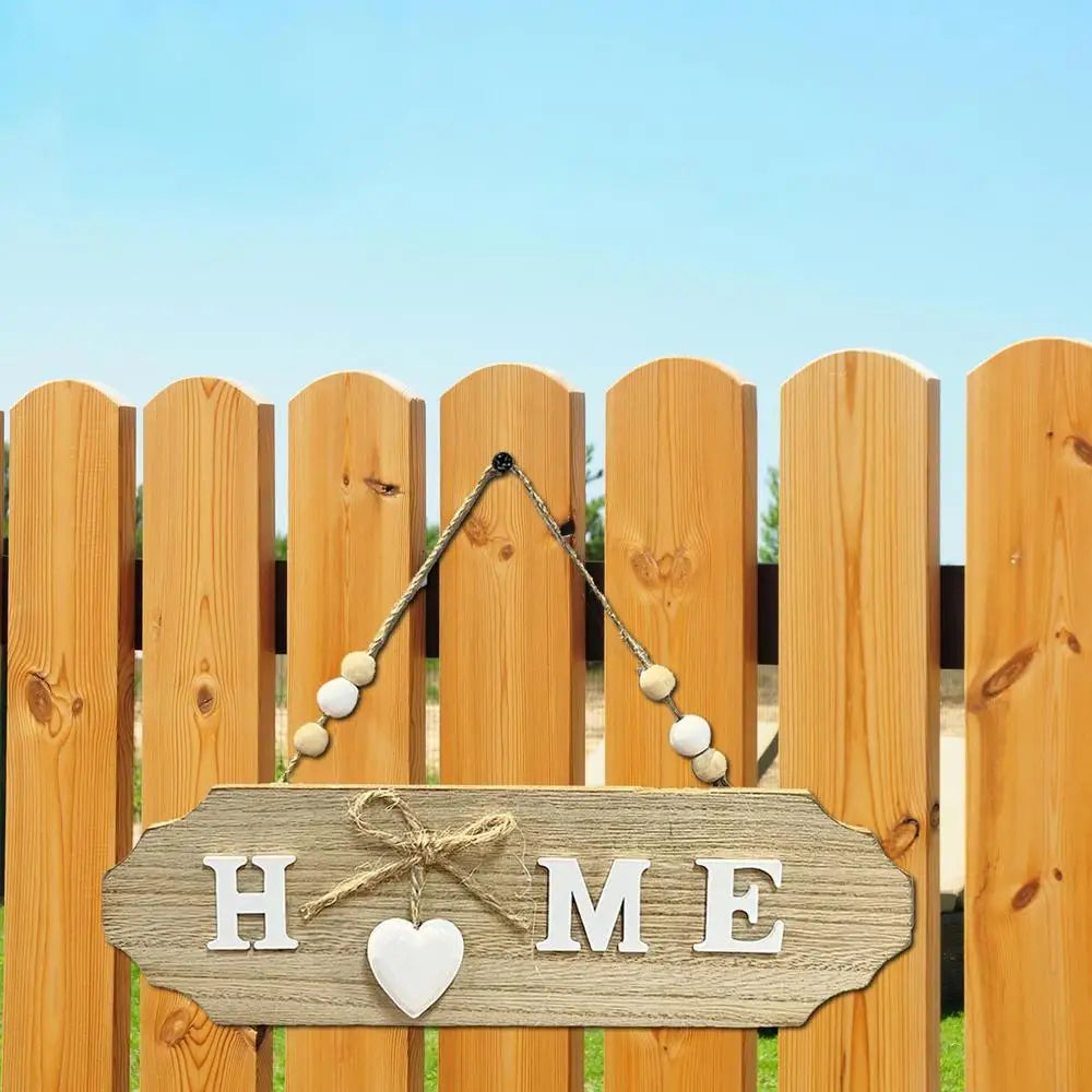 A wooden welcome sign with the words HOME carved into a plank, hanging on a vertical wooden fence.