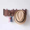A wooden wall coat rack with eight hooks displaying a straw hat and a fabric item.