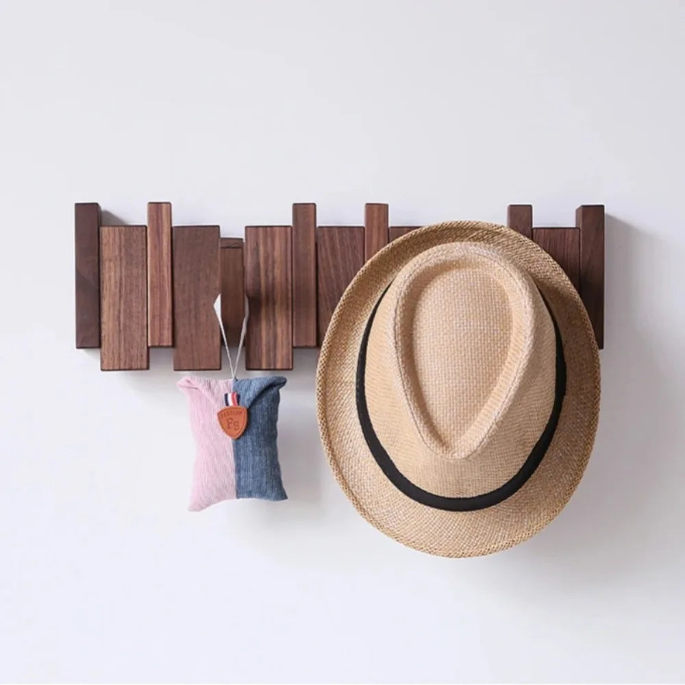 A wooden wall coat rack with eight hooks displaying a straw hat and a fabric item.