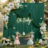 A green fabric backdrop with gold and white balloons, featuring the text Oh Baby, decorated with greenery and fairy wings.