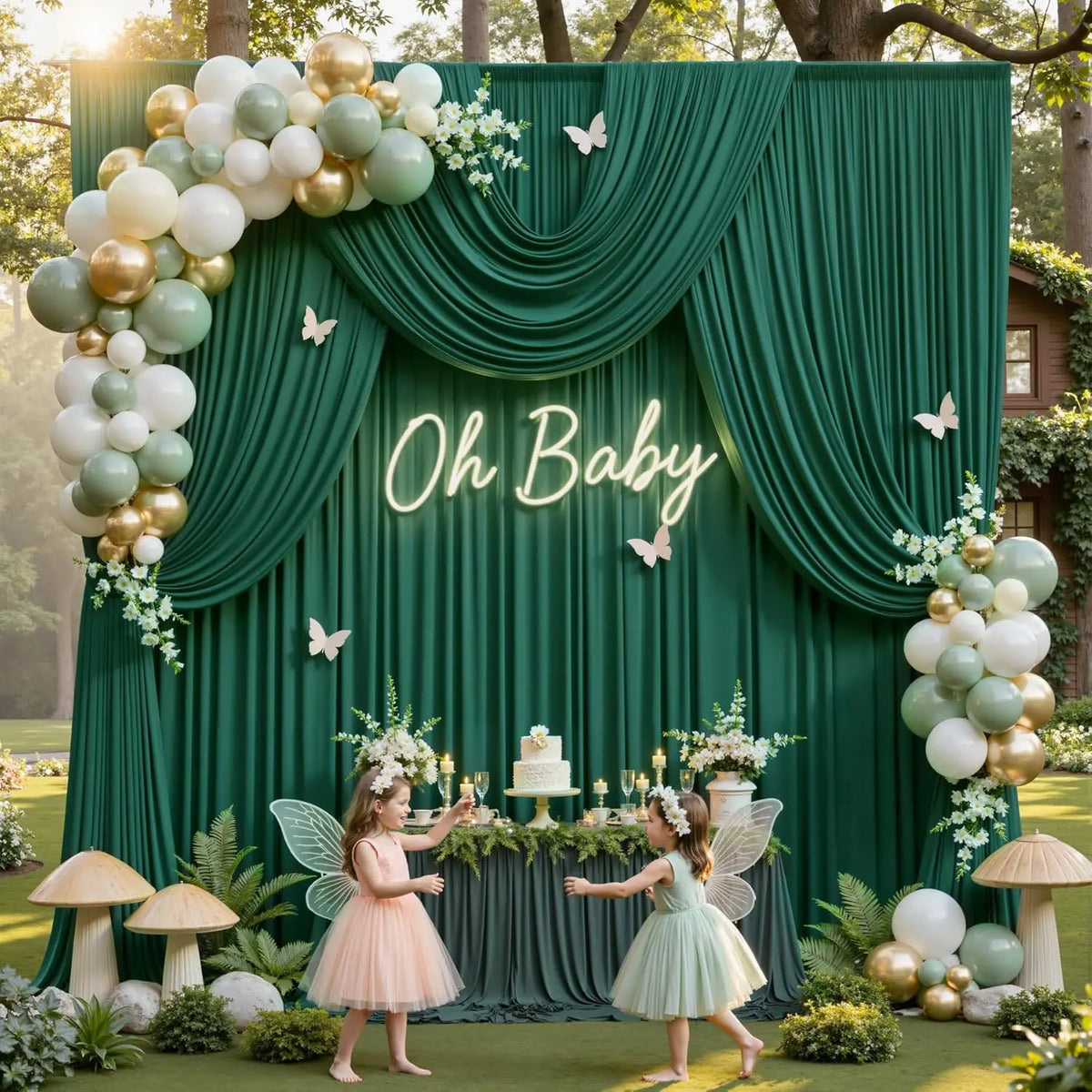A green fabric backdrop with gold and white balloons, featuring the text Oh Baby, decorated with greenery and fairy wings.