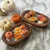 A wooden tray holds various orange and yellow pumpkin-shaped silicone molds and candle wax for a fall scented candle making k