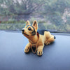 A small, tan and black dog ornament figure wearing a gold chain, resting on a dark surface.