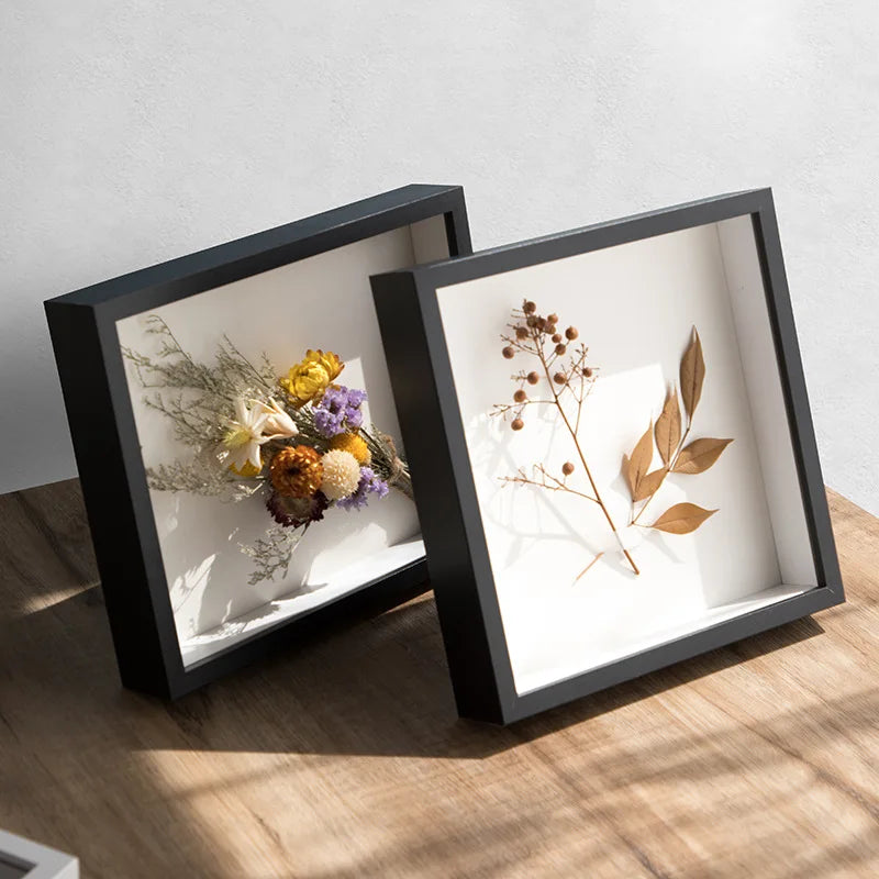 A black wooden shadow box photo frame displaying dried floral arrangements and botanical elements.