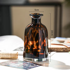 A dark amber glass vase with a leopard print pattern sits on a white surface.