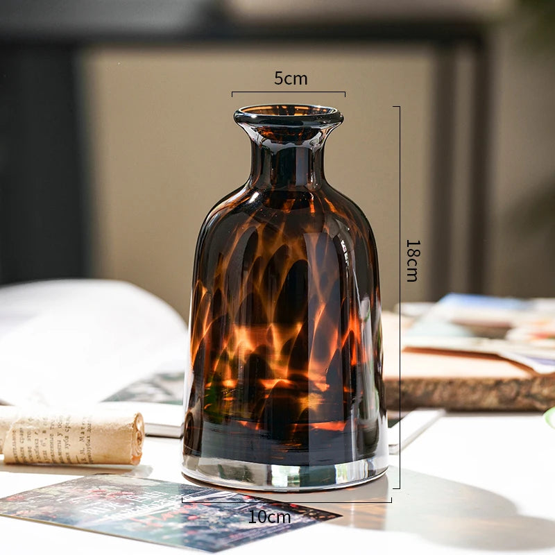 A dark amber glass vase with a narrow neck and rounded body sits on a white surface.
