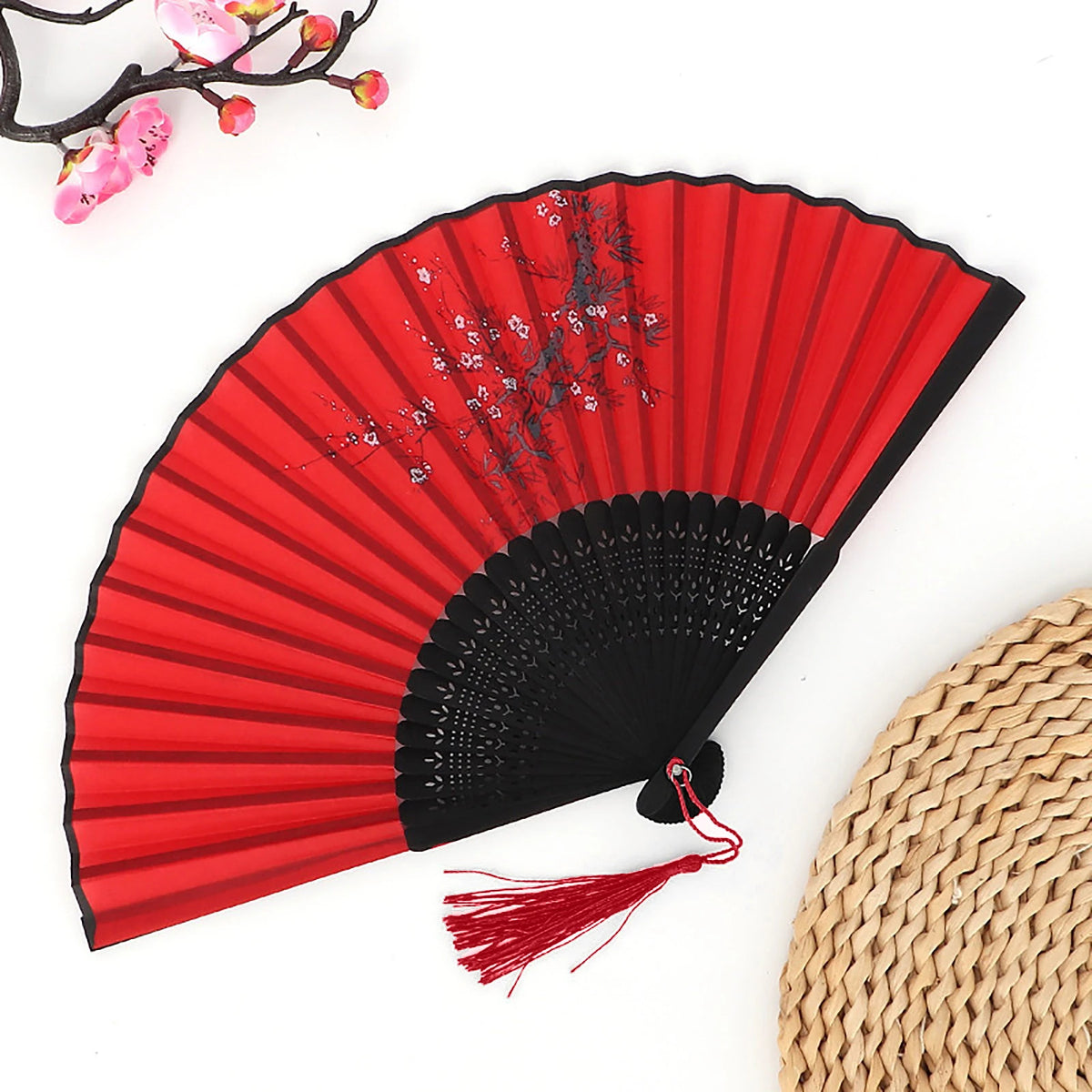 A red folding fan with black ribs and a bamboo handle is shown against a white background.