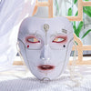 A white porcelain masquerade mask with intricate facial lines and red accents, displayed on a white cloth.