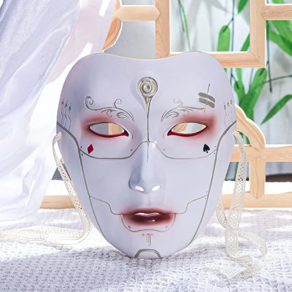 A white porcelain masquerade mask with intricate facial lines and red accents, displayed on a white cloth.
