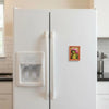 A white refrigerator door features a wooden frog photo frame magnet with pink hair styles.