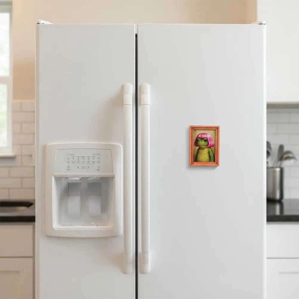 A white refrigerator door features a wooden frog photo frame magnet with pink hair styles.